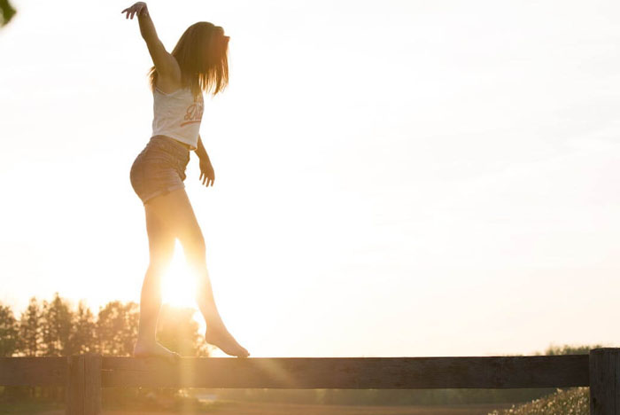 Femme pieds nus en équilibre sur une barrière, soleil couchant en arrière-plan