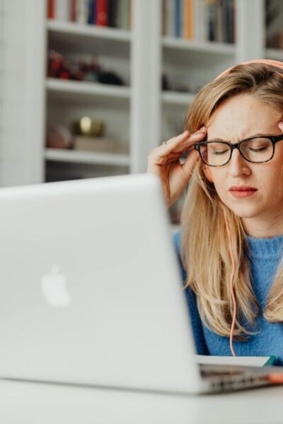 Femme assise devant un ordinateur qui se tient les tempes, décor de bureau.