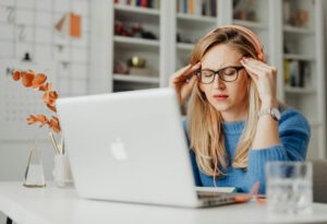 Femme assise devant un ordinateur qui se tient les tempes, fatigue, stress, décor de bureau