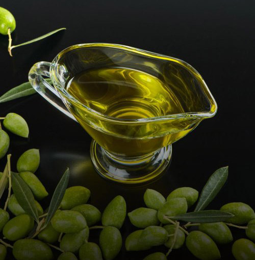 Huile d’olive dorée dans une verseuse en verre, feuilles et olives fraîches