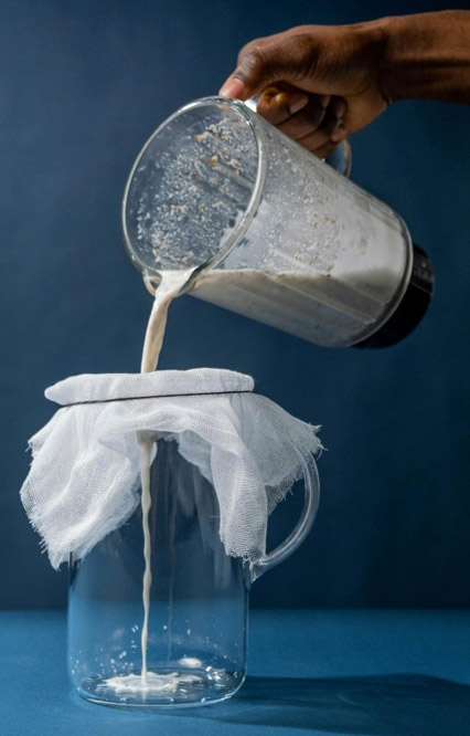 Tamisage du lait d'amande après mixage, sur fond bleu