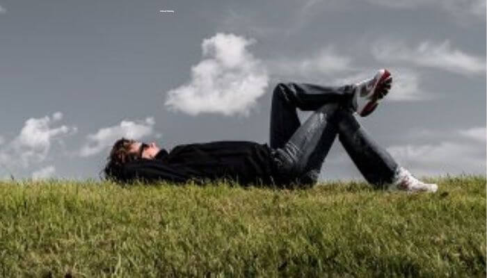 Personne allongée sur l’herbe, les yeux fermés — pour mettre le cerveau au repos et retrouver la paix intérieure