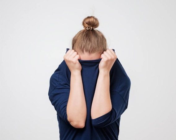 Femme debout cache son visage sous un pull bleu, peur-blog