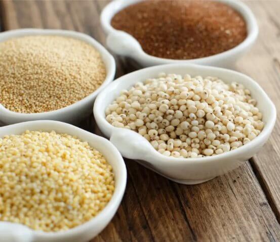 4 petits bols avec orge, millet, quinoa sur table en bois