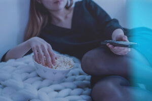 Femme allongée devant la télé la main dans un bol de popcorn