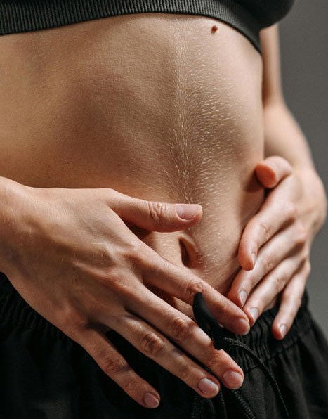 Digestion optimale. Femme posant ses mains sur son ventre — gros plan, vêtement sombre, posture apaisante