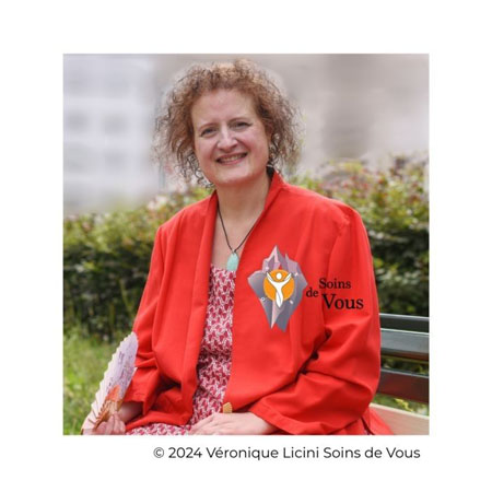 Véronique Licini, naturopathe et hypnothérapeute, souriante, veste rouge, collier avec pendentif, assise en extérieur
